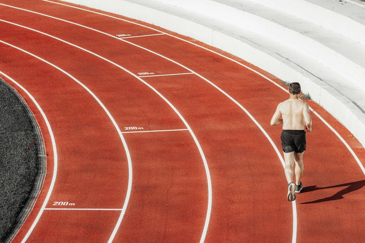 Coureur vu de dos dans un virage de piste d'athlétisme rouge